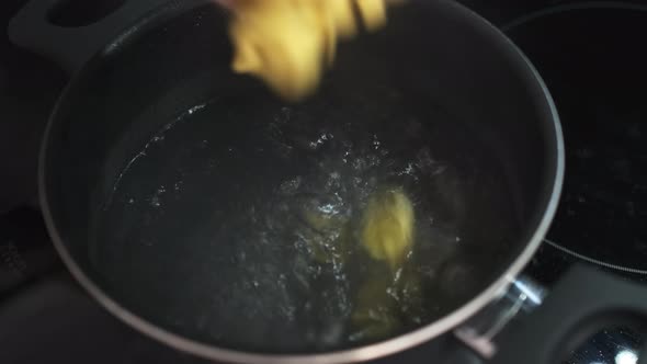 Woman Throws Raw Ravioli Into Saucepan with Boiling Water