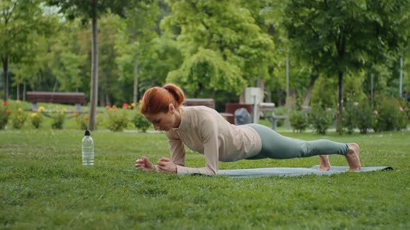 Woman standing in plank in the park on yoga mat, endurance effort