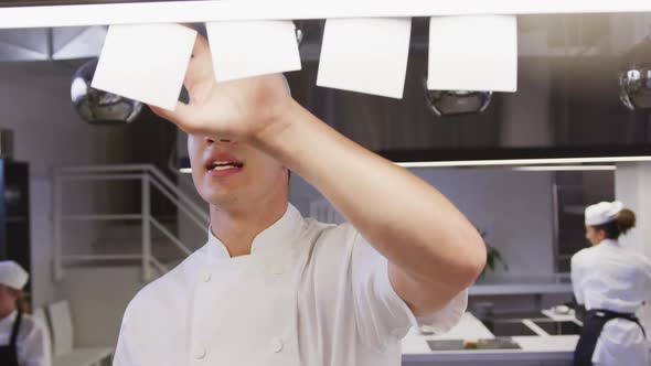 Caucasian male chef working in a restaurant kitchen checking orders, with colleagues working