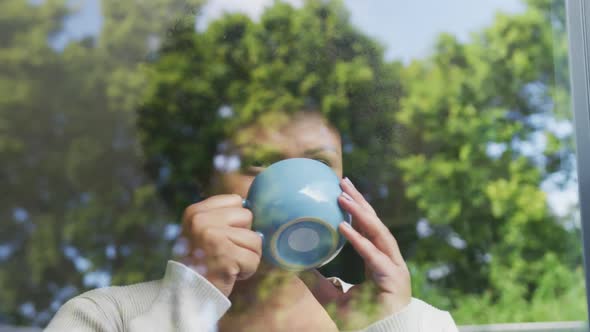 Video of relaxed plus size african american woman drinking coffee and looking outside window