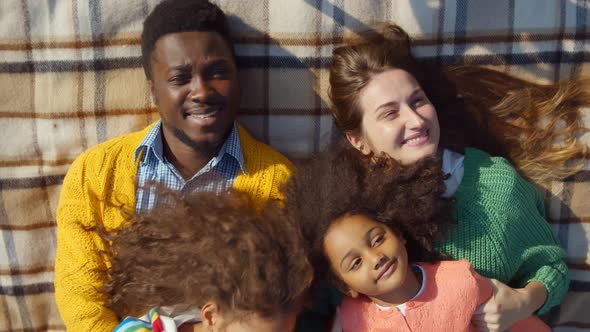 Multiethnic Family with Little Daughters Having Fun Together Resting on Checkered Blanket Outdoors