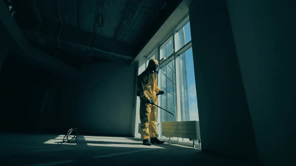 Worker in a Hazmat Suit is Sanitizing a Large Window