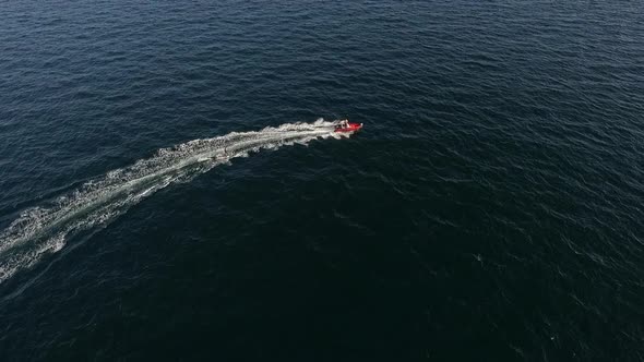 Flyover Drone Footage of Red Inflatable Boat with Motor and Man on It Pulling Another Male on Board