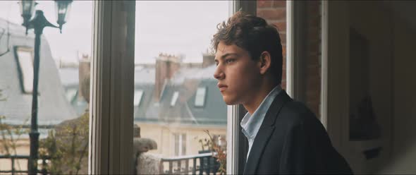 Melancholic young man looking out the window on a cloudy day