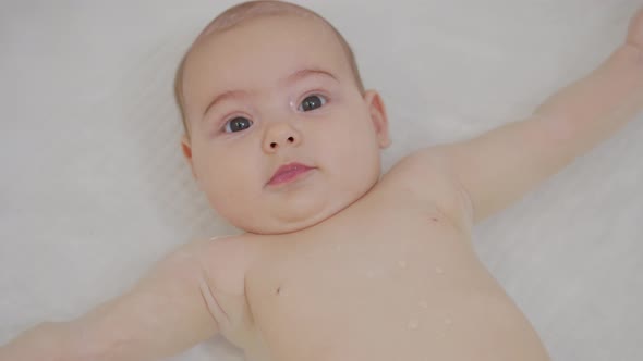A Nice Little Caucasian Newborn Baby Is Funny Smiling, Lying at the Back in the Bath, Portrait 
