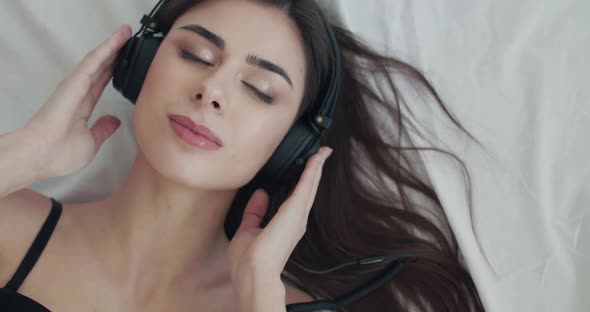 Girl Listening to Music on Bed Flirts Into Camera and Twists Headphones' Wire