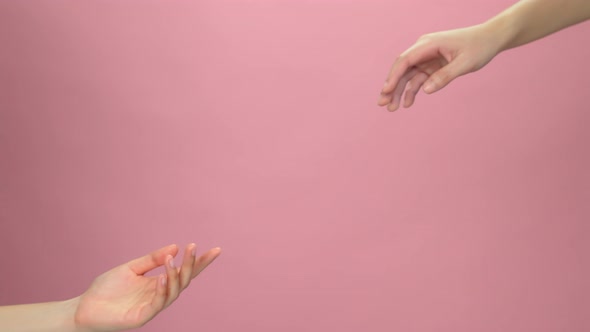 Close up of two hands touch the fingertips on light pink background.