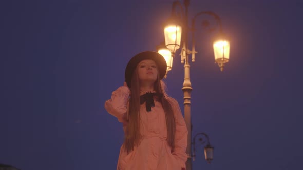 Woman Adjusts Hat Posing for Photo Against Bright Lantern