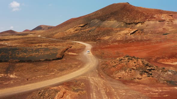 One White SUV Car Driving Alone Travel on Empty Dirt Road Freeway Through Desert Volcanic Landscape