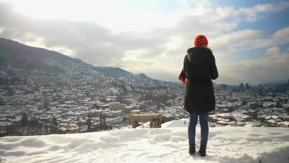 Back View of blonde woman in a blue winter coat staring at the Neretva River in Mostar