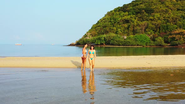 Young smiling ladies relaxing having fun on beach on paradise white sand and blue 4K background