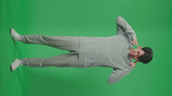 Full Body Of Stressed Asian Man Covering Her Ears While Standing In Front Of Green Screen Background