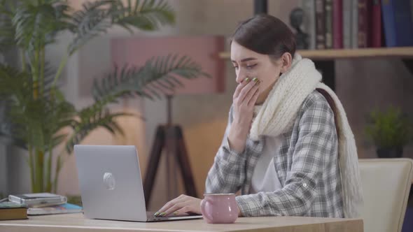 Portrait of Brunette Caucasian Woman in White Scarf Coughing and Typing on Laptop Keyboard. Young