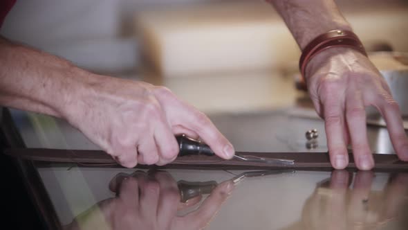 The Tailor Cuts Off the Piece of Leather By the Table Using a Sharp Instrument