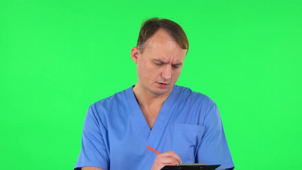 Medical Man Fills Papers at Black Folder with Pencil, Green Screen