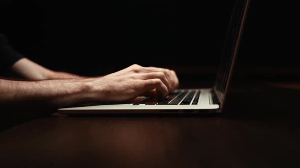 Dollyin Shot of Young Man Working Typing on Keyboard Laptop Computer at Dark Room Closeup