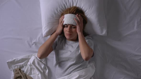 Young Woman Suffering From High Fever, Lying in Bed With Compress on Forehead