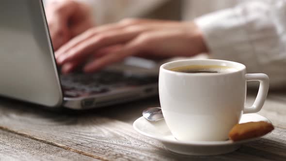 An Office Worker Works Behind A Portable Laptop In The Foreground A White Cup Of Black Coffee