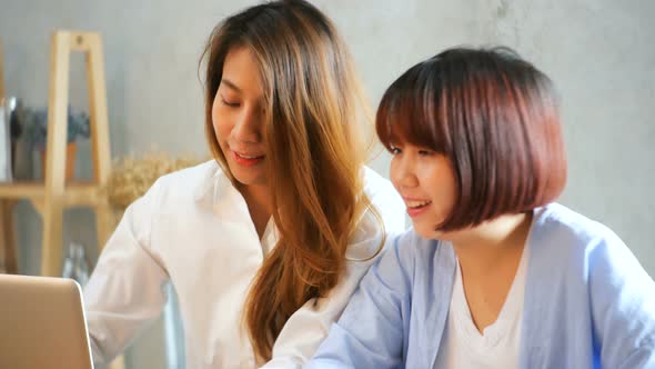 Two young business women sitting at table in cafe. Asian women using laptop and cup of coffee.