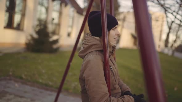 Young Attractive Redhaired Woman Swinging on a Swing in the City at Sunset or Sunrise