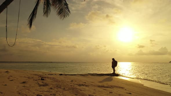 Backpacker standing over big rock on exotic beach under a palm tree at sunset moments with yellow sk