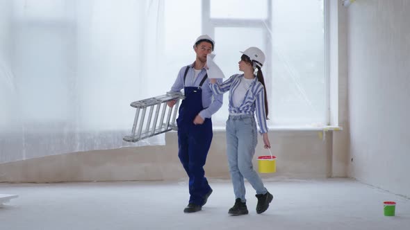 Woman in Protective Helmets with Stepladder and Bucket of Paint in Their Hands Discussing Color