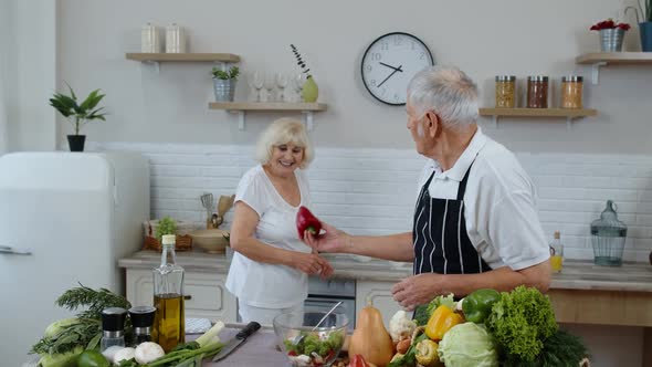 Senior Vegan Grandmother and Grandfather Cooking Salad with Fresh Vegetables in Kitchen at Home