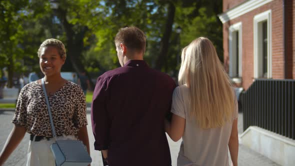 Back View of Young Man Walking with Girlfriend and Looking at Another Woman Passing By