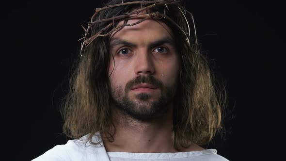 Crying Jesus Christ in Crown if Thorns Looking at Camera Against Dark Background