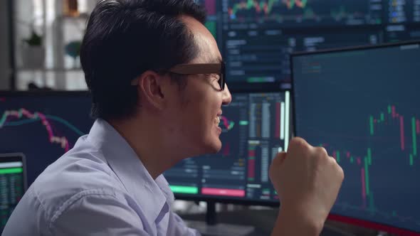 Asian Male Stock Market Broker Celebrating With Analyzing Graphs On Multiple Computer Screens