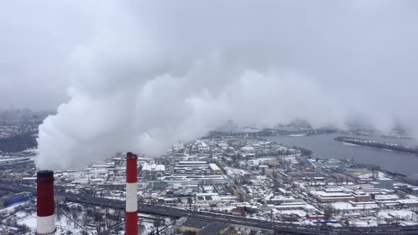 Aerial Survey Over the Tops of Two Smoking Factory Pipes and the Snow-capped City Lying Below. alt