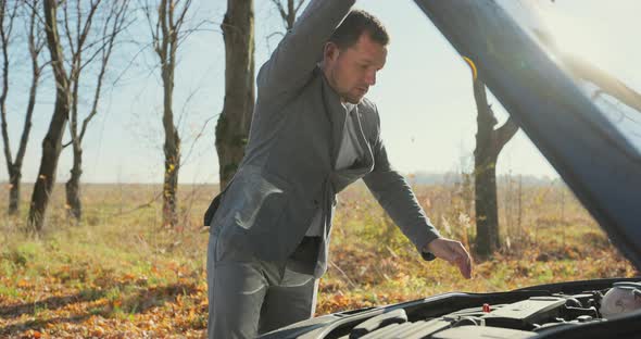 Worried Man in a Safety Vest Holding His Head By Hand Standing Near His Broken Car with Raised Hood