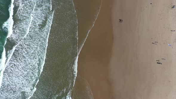 Top down aerial shot of a warm tropical beach with waves gently crashing onto the shore.