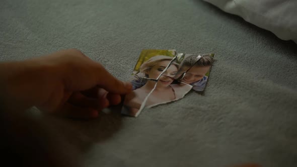 Hands of Young Male Trying to Put Together Parts of Torn Photo With Girlfriend