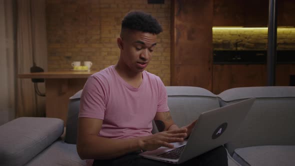 Young African American Man Talking By Video Call Using Laptop Sitting on Couch at Home