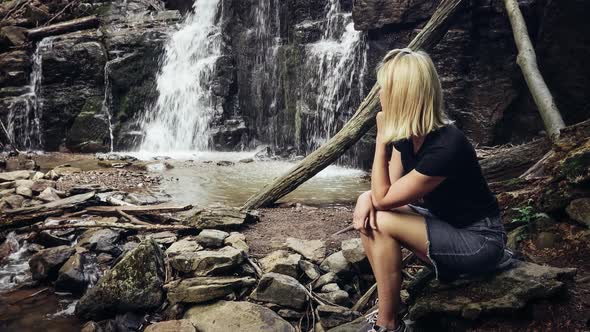 girl sitting near the waterfall and enjoys the sounds of water