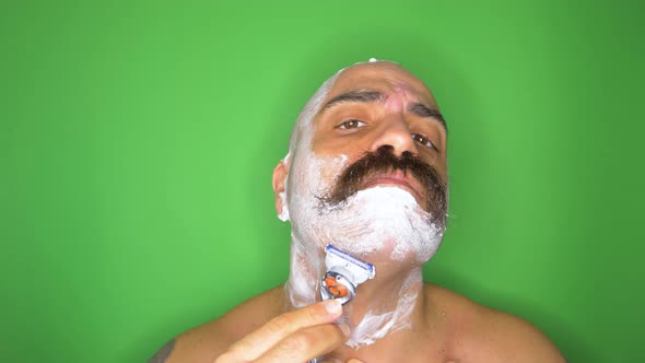 Portrait of man shaving his beard and head in front of a green wall