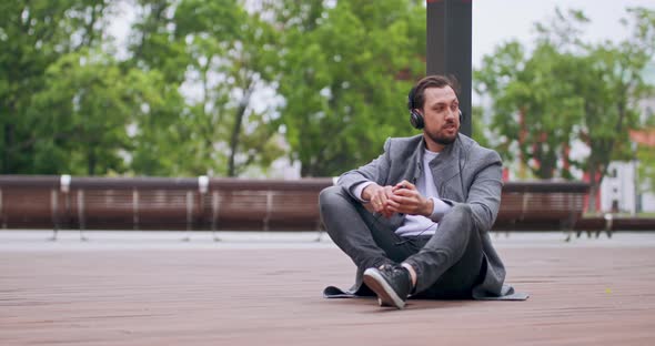 Young Man with Mustaches and a Beard Who Sits on the Wooden Floor in the Square Leaning His Back