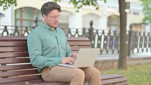 Man Thinking while Working on Laptop on Bench