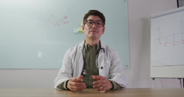 Portrait of asian doctor smiling and waving on video call looking at the camera
