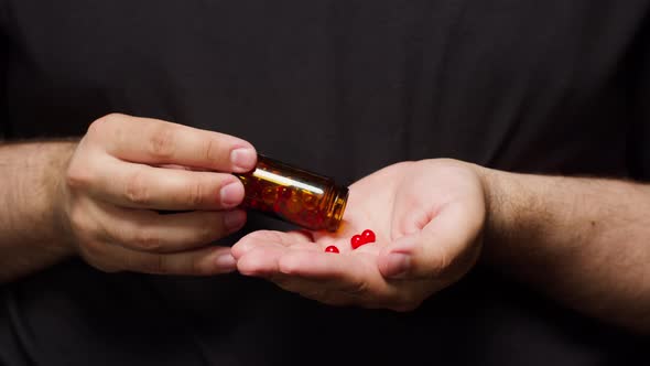 Man Wearing Black Tshirt Putting Medicine Tablets Into Hand Shooting of Pouring Out Red Drugs in