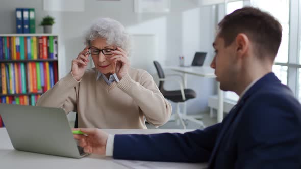 Young Specialist Consult Aged Client and Showing Insurance Program on Laptop