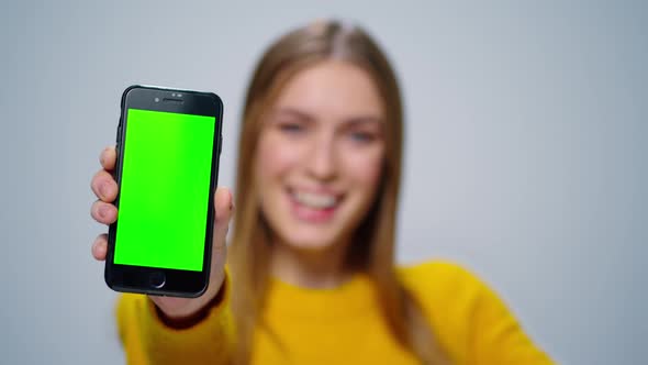 Smiling Woman Showing Smartphone with Green Screen in Studio