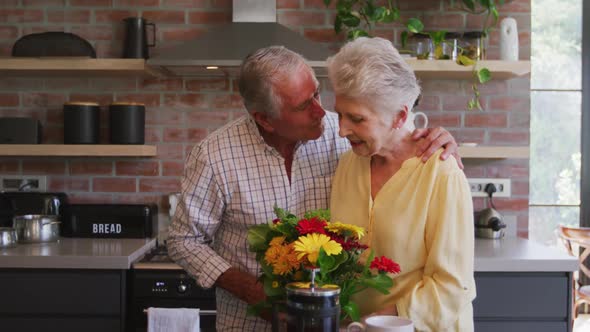 Senior Caucasian husband offering flowers to his wife, hugging and smiling