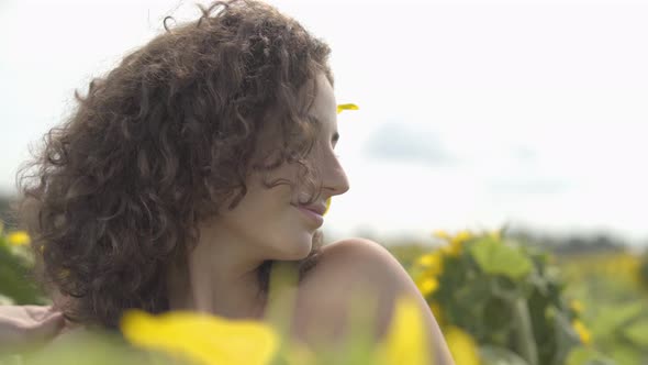 Portrait of Cute Curly Playful Girl Looking at the Camera Smiling Standing in the Sunflower Field