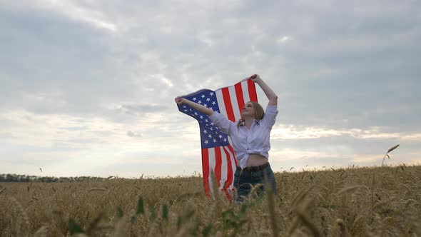 Happy Patriotic Young Woman Waves the US Flag Into the Field