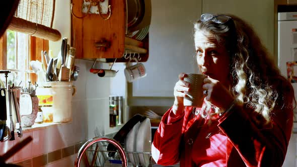 Mature woman having coffee in kitchen 4k