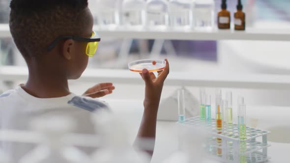 Video of happy african american boy wearing glasses and holding reagent during chemistry lesson