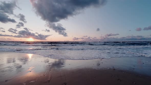 The waves of the sea smoothly spread along the sandy shore at sunset. Sunset at the sea.