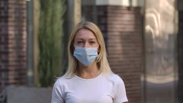 Portrait of Pretty Young Woman in Medical Mask Looking Into the Camera. Blonde in a White Blouse